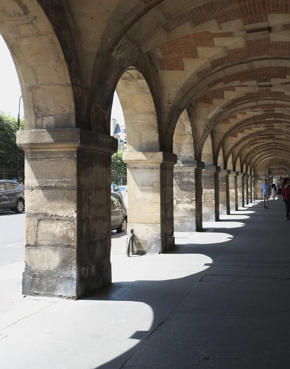 Arcades de la place des Vosges, à Paris, où passent des visiteurs.